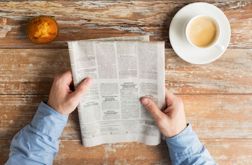 close up of male hands with newspaper and coffee newspaper in hands with coffee and muffin