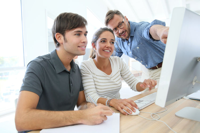 Teacher with group of students in class working on desktop people training in front of a computer